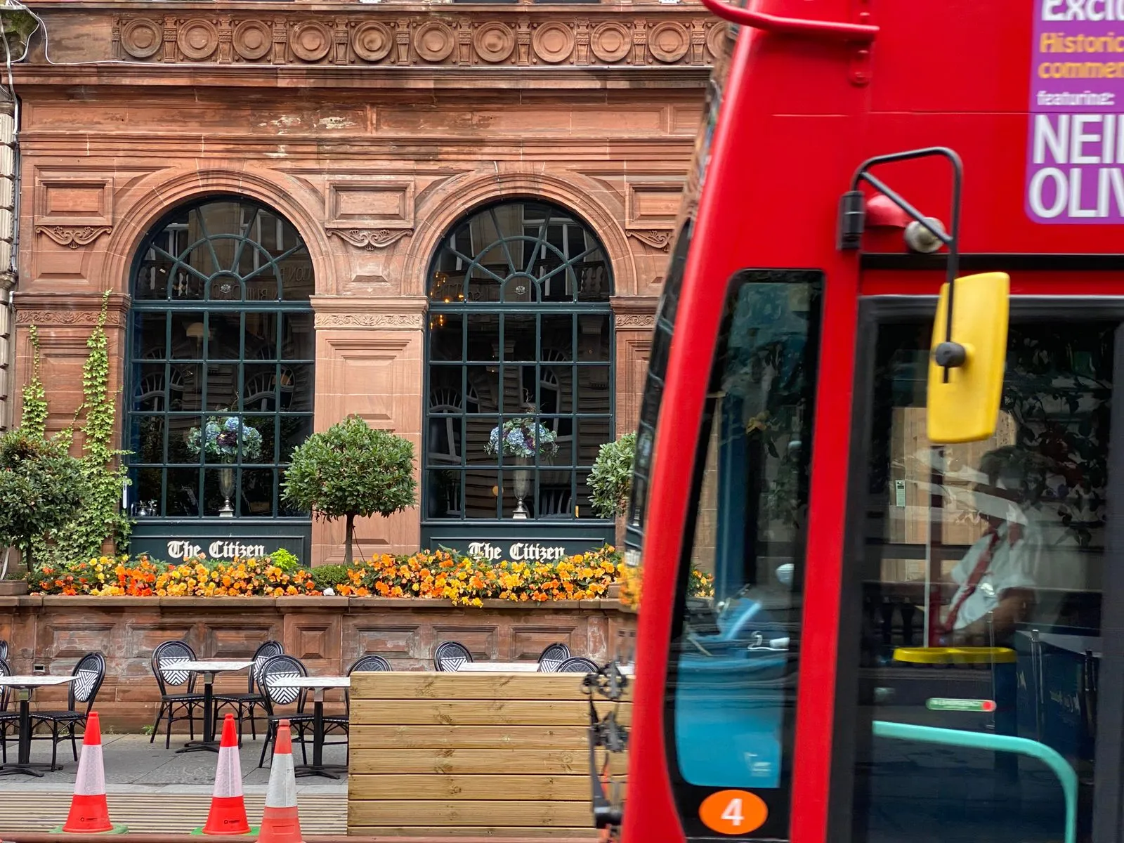 A vibrant city street featuring a historic building facade and a classic red bus in Glasgow, Scotland.